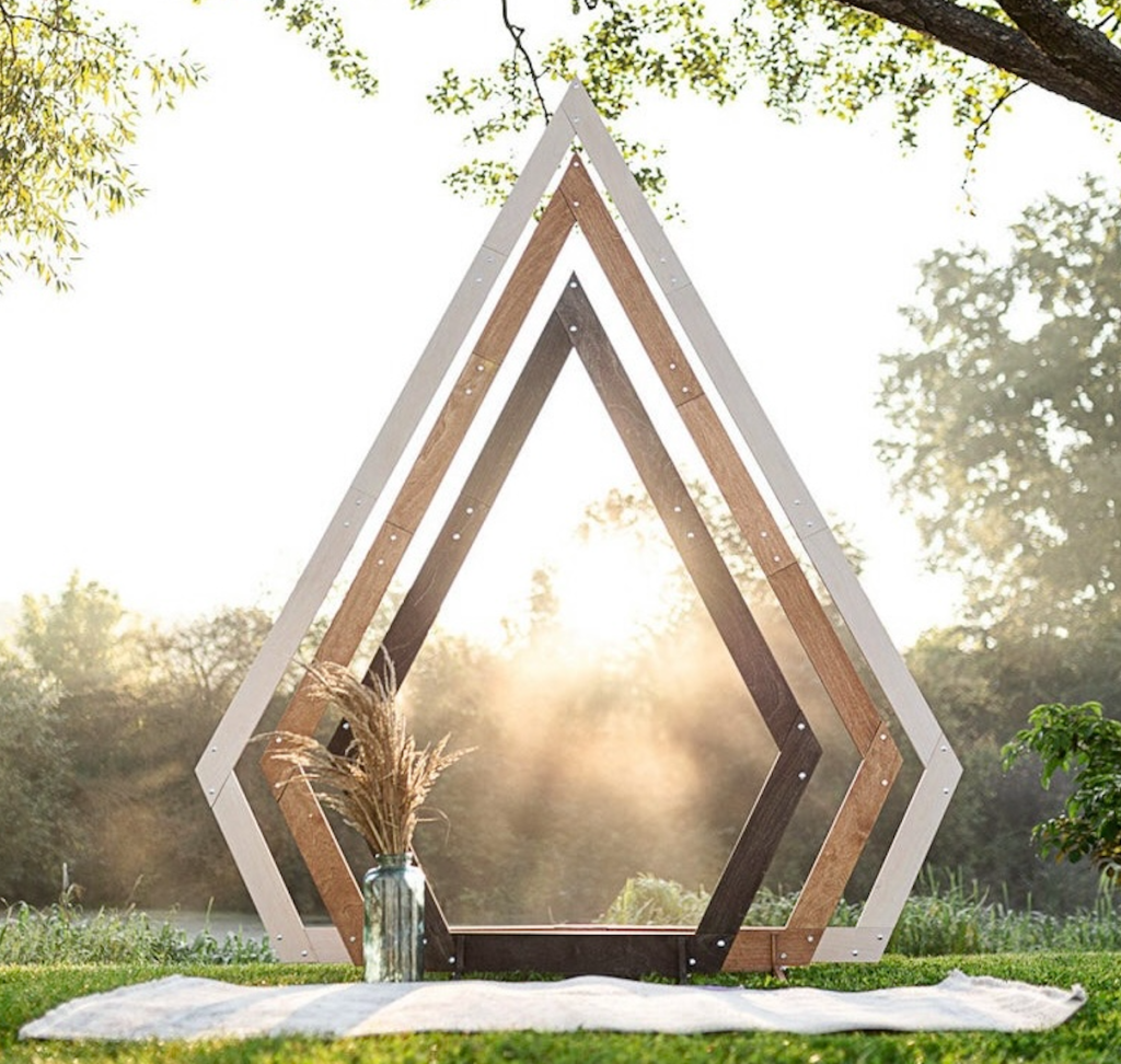 A geometrical, wodden archway in an outdoor setting set up for a wedding or special event.